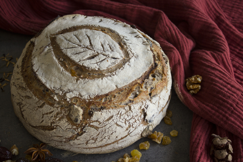 Round artisan bread on a red kitchen towel. Beautiful homemade bread with raisins and nuts. Rustic style still life. 