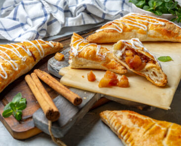 Apple turnovers and cinnamon sticks on a wooden serving board, selective focus.