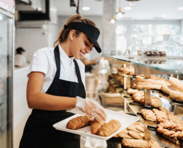 Beautiful young and happy female worker working in a modern bakery or fast food restaurant.