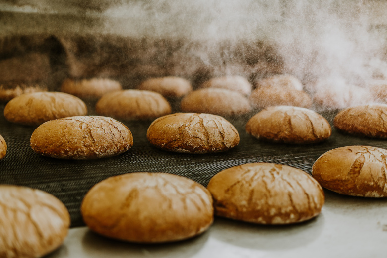 Fresh buns from the oven. Conveyor with bread. Baking bread. Workshop for production of bread. White bread in the oven. Hot buns. Confectionery