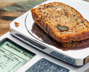 slice of banana bread with walnuts on diet scale displaying nutrition facts - a diet concept