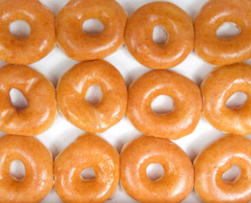Top view flat lay of plain glazed donuts in a white box isolated. One dozen donuts. The original glazed donut has remained peoples favorite throughout history.