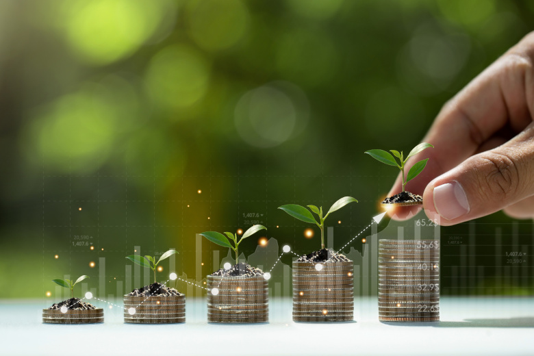 Hand putting coins on a stack with plant growing on the money wi