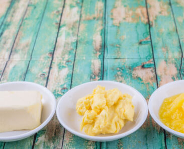 A block of butter, margarine and ghee in white bowls over rustic